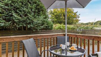 A wooden deck with a round glass table, two chairs, and an umbrella.