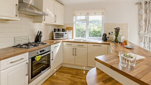 A modern kitchen with white cabinetry, a gas stove, an oven, a microwave, and a window with a view of greenery.