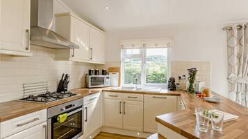 Une cuisine moderne avec des meubles blancs, une cuisinière à gaz, un four, un four à micro-ondes et une fenêtre donnant sur un paysage verdoyant.