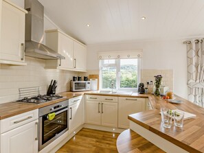 A modern kitchen with white cabinetry, a gas stove, an oven, a microwave, and a window with a view of greenery.
