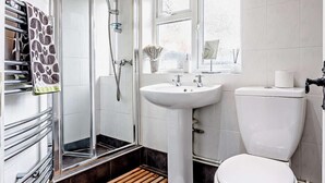 Un bany amb un plat de dutxa de vidre, un lavabo blanc, un vàter i una finestra amb vistes.