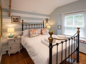 Een slaapkamer met een bed, nachtkastje, bedlampen en een raam met zonwering.
