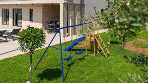 A modern outdoor area with a swing set, a slide, and a seating area with chairs and a table. - Villa Moon - SeaView&Hydromassage by Villas Guide (Peruški)
