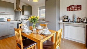 Une cuisine moderne avec des meubles gris, une table à manger en bois pour quatre personnes et une machine à café posée sur le plan de travail.