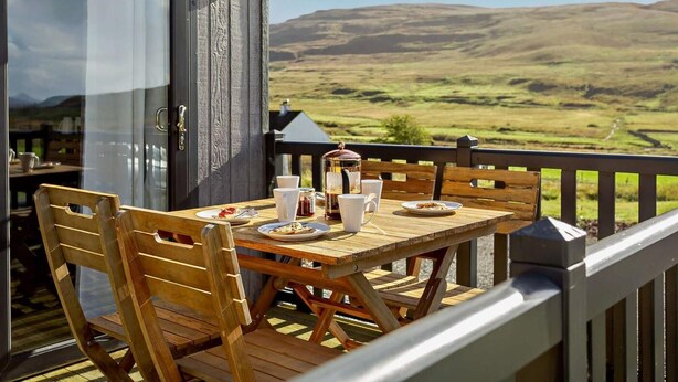 Une table en bois, entourée de chaises, sur un balcon offrant une vue magnifique.