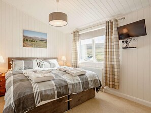 A bedroom with a bed, a window with curtains, a television mounted on the wall, and a painting on the wall.