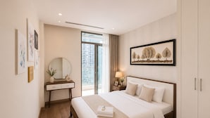 Et hotelværelse med en seng, et skrivebord med et spejl, et natbord med en lampe og et vindue med udsigt til bygninger.