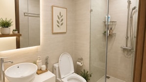 Et moderne badeværelse med en glasafskærmet brusekabine, en hvid vask og et toilet.