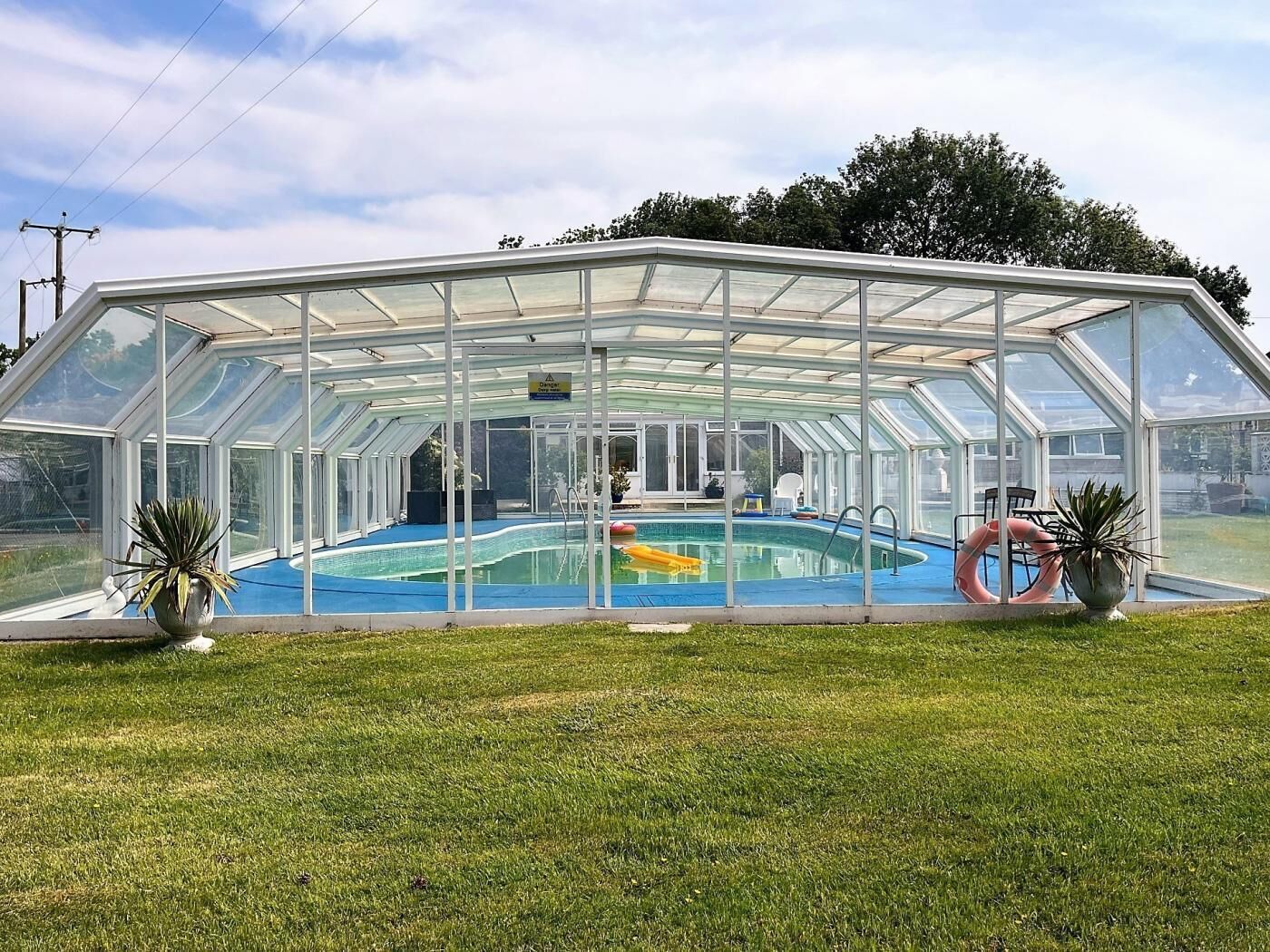 A glass-enclosed swimming pool with a clear roof, surrounded by grass.