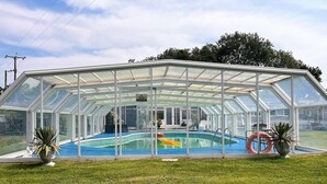 Una piscina con techo transparente y paredes de vidrio, rodeada de césped.