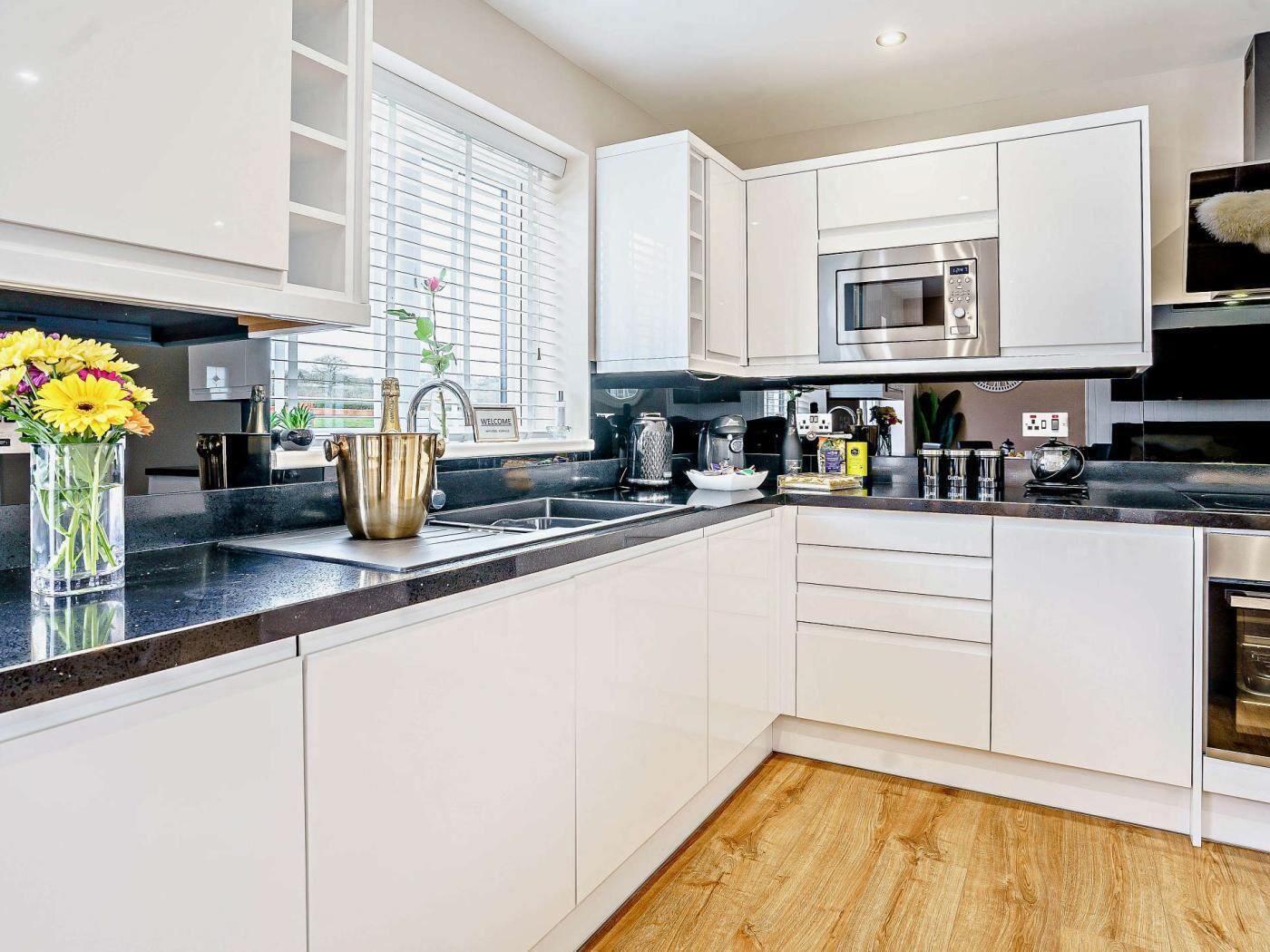 A modern kitchen with white cabinetry, a built-in microwave, and a wooden floor.