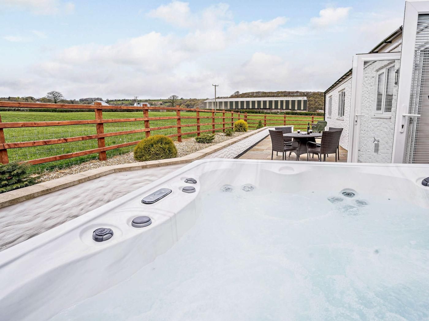 A hot tub with controls, a wooden fence, and a building in the background.