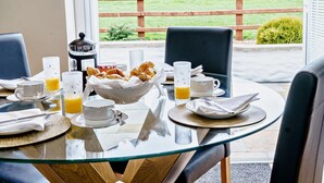 Una mesa de desayuno con cruasanes, jugo de naranja y tazas de café, frente a una vista de un campo verde y una valla de madera.