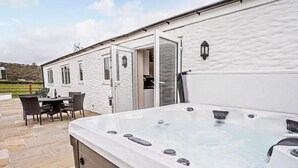 Un jacuzzi con un patio de piedra, un edificio blanco con una puerta y una mesa con sillas.