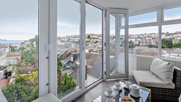 Ein Balkon mit Tisch, der für Tee gedeckt ist, einem Korbsessel und Blick auf die Stadt.