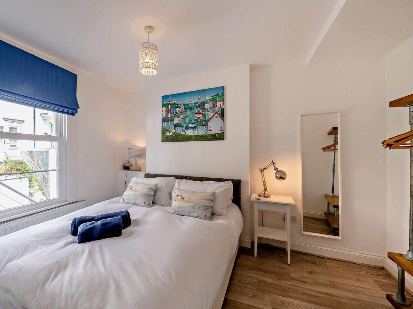 Een slaapkamer met een bed, een schilderij, een nachtkastje, een lamp en een spiegel.