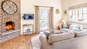 A living room with a brick fireplace, a flat-screen TV, a sofa, and a window with a view of the outdoors. - 2 Bed in Dorchester (oc-75243) (Sydling Saint Nicholas)