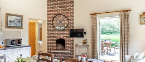 A dining area with a brick fireplace, a television mounted above it, and a view of the outdoors through large windows.
