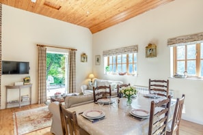 A dining area with a table set for four, wooden chairs, a television on a stand, and a view of the outdoors through a window. - 2 Bed in Dorchester (oc-75243) (Sydling Saint Nicholas)