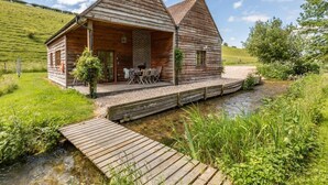 A wooden cabin with a porch, outdoor seating, and a dock over a stream. - 2 Bed in Dorchester (oc-75243) (Sydling Saint Nicholas)