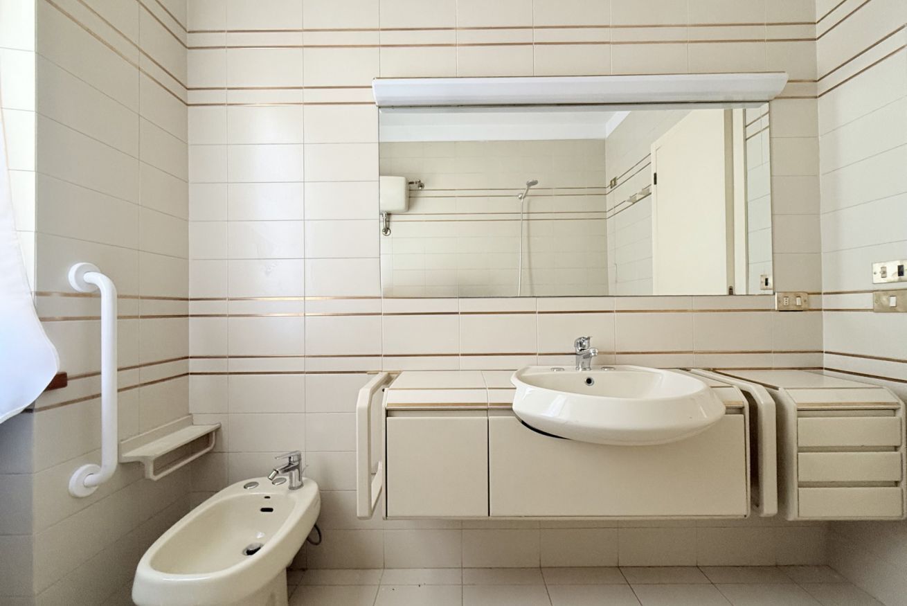 Ein Badezimmer mit Bidet, zwei Waschbecken, einem Spiegel und einem Handtuchhalter.