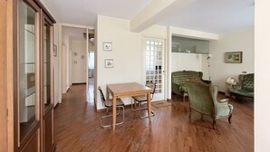 Une pièce spacieuse avec un plancher en bois, une table à manger avec des chaises, un canapé vert et un miroir au mur.