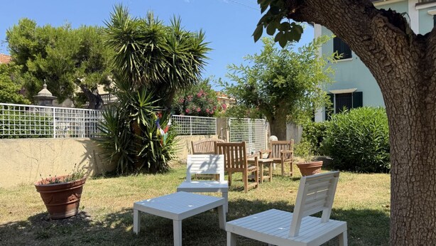 Une terrasse avec des meubles blancs, un arbre et une clôture.