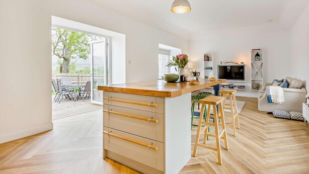 Een moderne keuken met een houten eiland, barkrukken, een televisie en een eetgedeelte met stoelen.