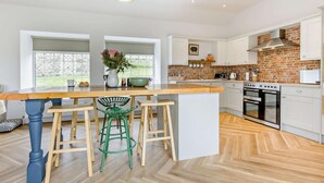 Een moderne keuken met een groot eiland, witte keukenkastjes, een tegelwand van baksteen en een hangende hanglamp.