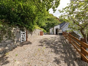 A gravel driveway leading to a building with a stone wall and a wooden fence.