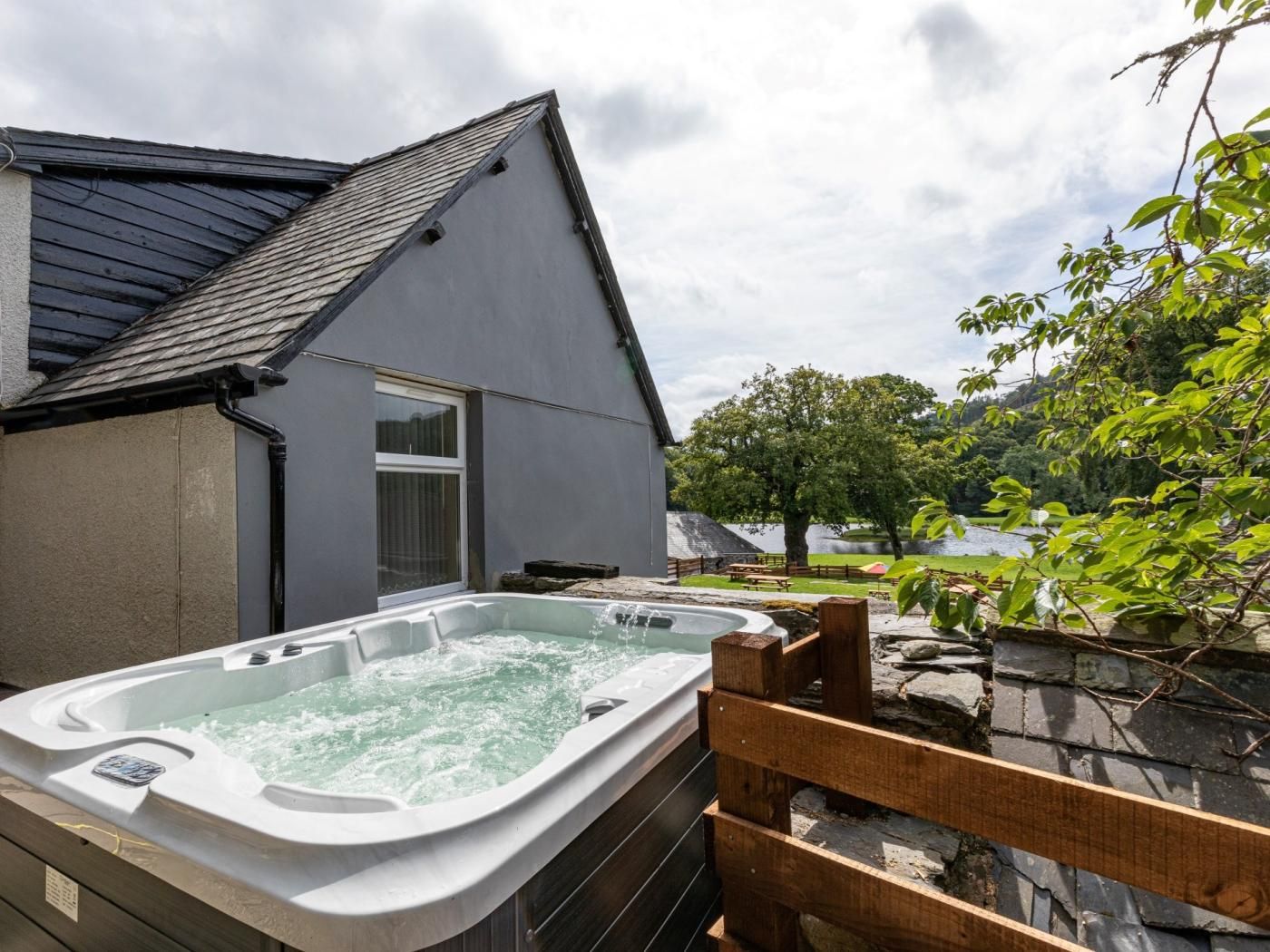 A hot tub in a backyard with a house, a wooden deck, and a lake view.