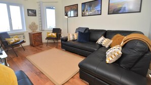 A living room with a black leather sofa, a wooden coffee table, and a large window.