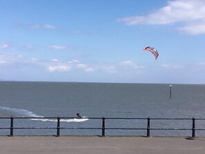 A coastal view with a person windsurfing, a railing, and a distant buoy.