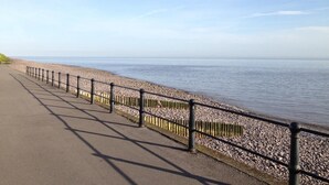 A paved walkway alongside a pebble beach with a metal railing.