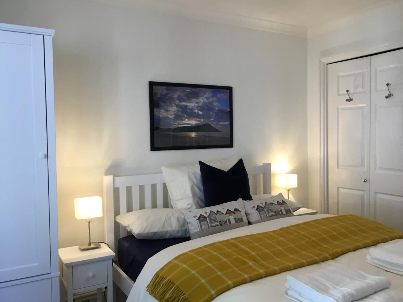 A hotel room with a bed, bedside lamps, a nightstand, a wardrobe, and a framed picture on the wall.