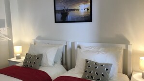 A hotel room with two beds, white headboards, and a nightstand with a lamp. - 2 Bed in Minehead (oc-75338) (Minehead)