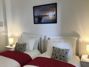 Ein Hotelzimmer mit zwei Betten, weißen Kopfteilen und einem Nachttisch mit Lampe.