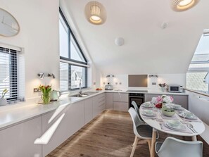 A modern kitchen with a dining area, large windows, and a sloped ceiling. - 3 Bed in Bideford (oc-75345) (Northam)