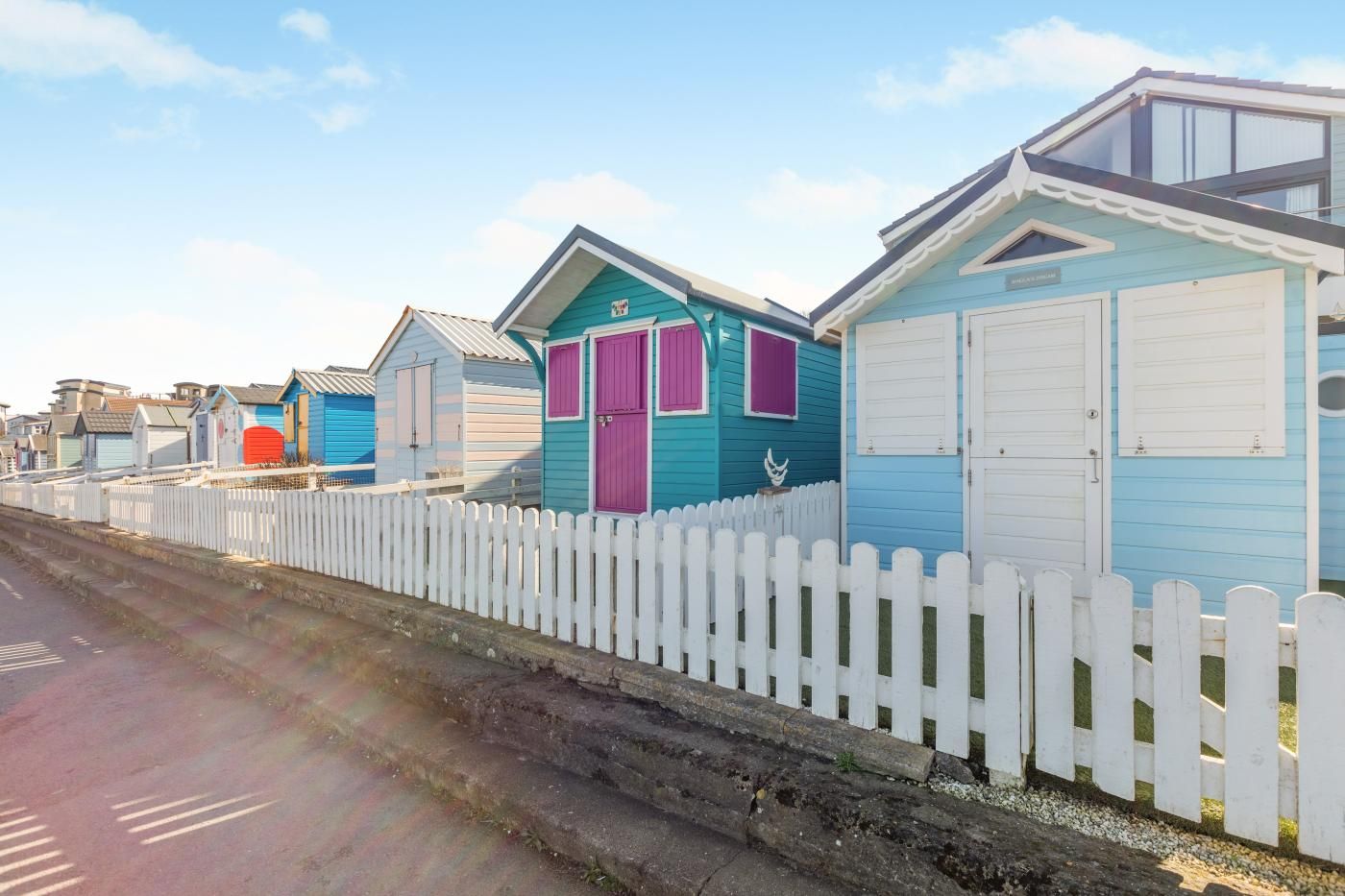 A row of beach huts with white picket fences, each with a distinct color and a garage door.