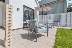 Eine Terrasse mit Gartenmöbeln, einem weißen Zaun und einem Stapel Holzklötze.