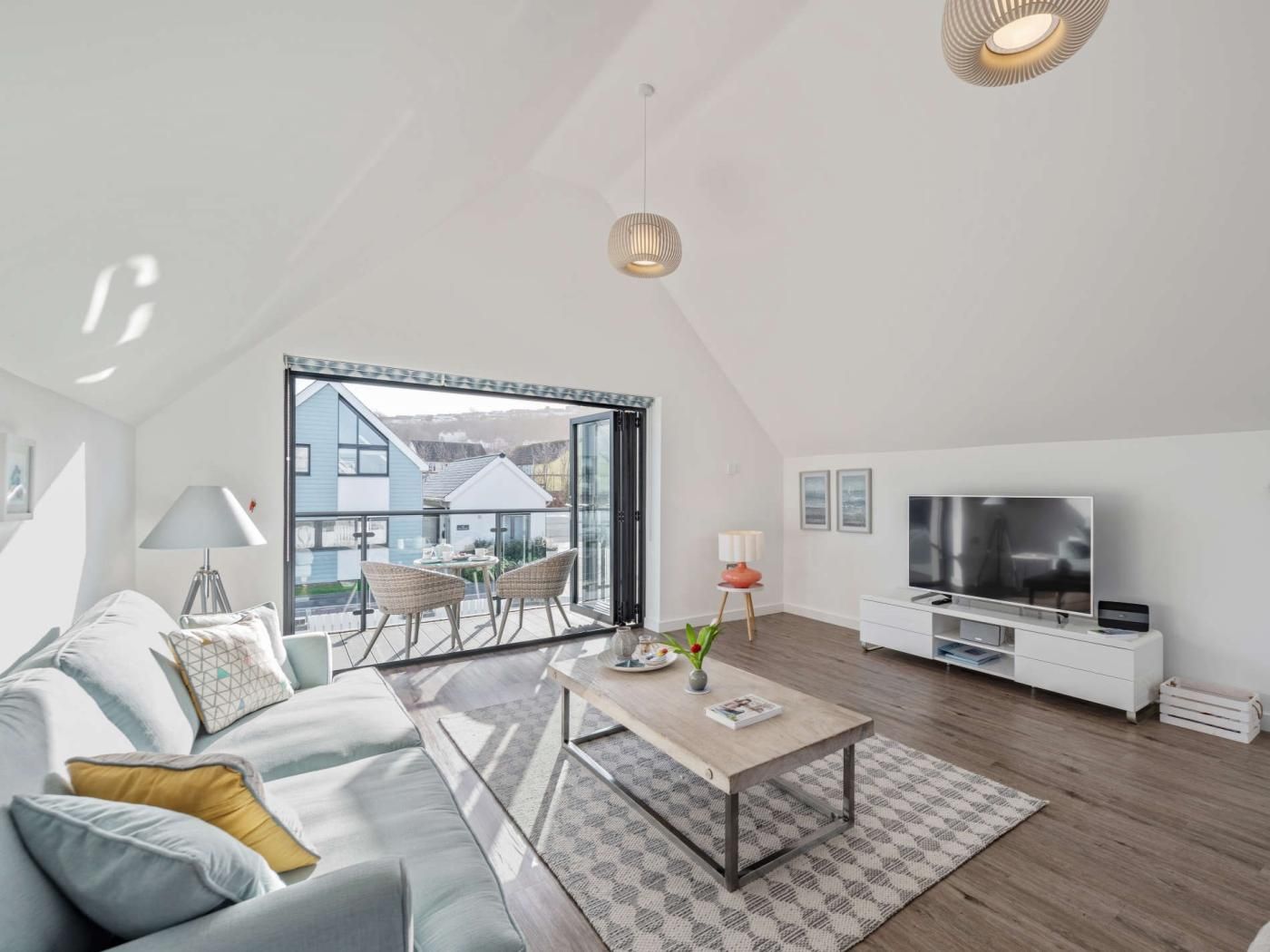 A modern living room with a sofa, coffee table, TV, and a balcony with a view of houses.