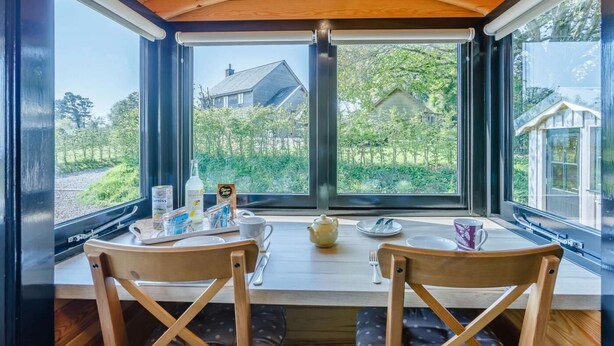 Ein Essbereich mit Tisch, Stühlen und Blick auf einen Garten durch große Fenster.