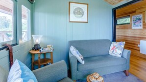 Ein gemütliches Zimmer mit Holzboden, blauer Wand, grauem Sofa, kleinem Tisch mit Lampe und einem Poster an der Wand.