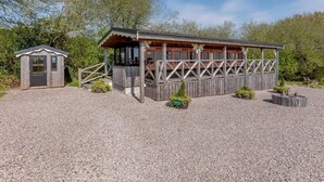 Ein Holzhaus mit einer überdachten Veranda, einem kleinen Nebengebäude und einem Schotterweg.