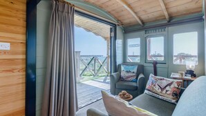 Ein gemütliches Zimmer mit Holzbalkendecke, einem Fenster mit Aussicht, einer Couch mit Kissen und einem Tisch mit Lampe.