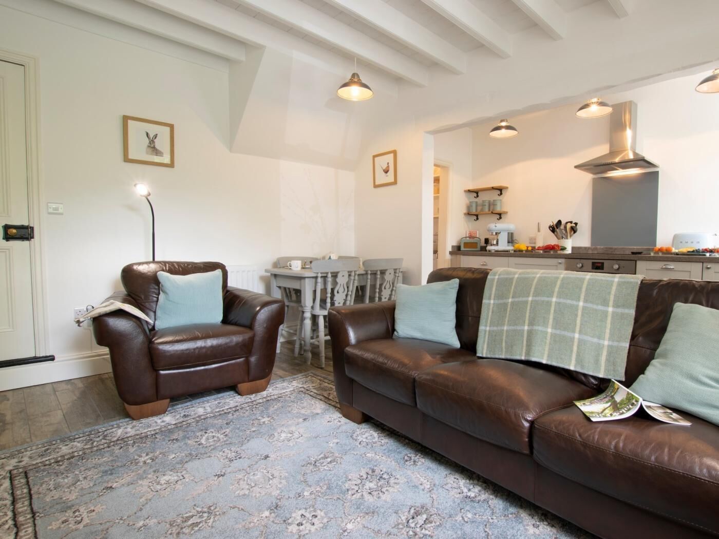 Ein Wohnzimmer mit braunem Ledersofa, einem Couchtisch und einem Esstisch mit Stühlen. Es gibt eine Küchenzeile mit Herd und Schränken.