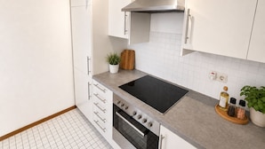 A modern kitchen with white cabinets, a stainless steel range hood, a black induction cooktop, and a built-in oven. - BS1 Property 29 B/C Near Wiesbaden (Wiesbaden)
