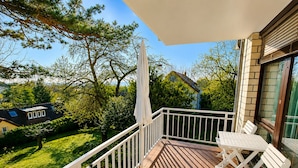 A balcony with a white railing, a table, and chairs, overlooking a green lawn and neighboring houses. - BS1 Property 29 B/C Near Wiesbaden (Wiesbaden)