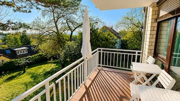 Ein Balkon mit weißer Reling, Tisch und Stühlen mit Blick auf eine grüne Rasenfläche und angrenzende Häuser.