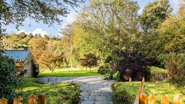 Een pad van stenen loopt door een tuin, met een houten omheining aan één kant en een tuinhuis aan de andere kant.